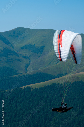A paraglider flies over a mountain valley on a sunny summer day. Paragliding in the Carpathians in the summer.