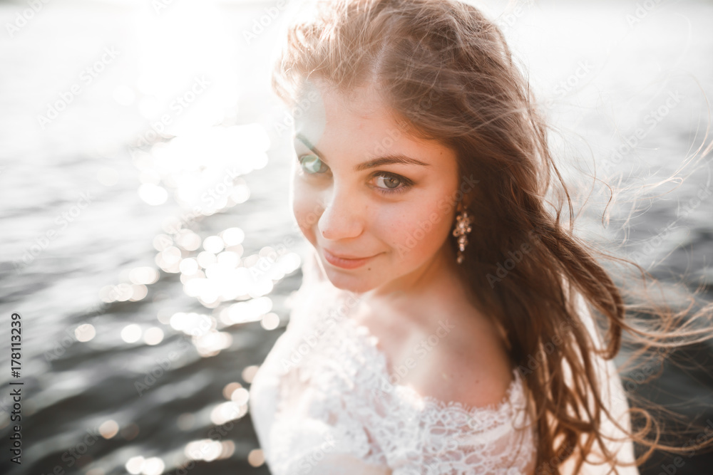 Pretty lady, bride posing in a wedding dress near sea on sunset Pretty lady, bride posing in a wedding dress near sea on sunset