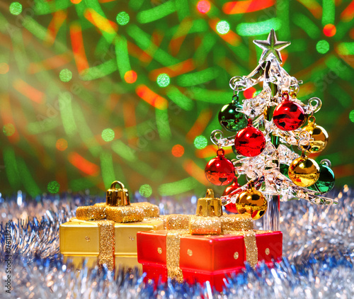 Glass christmas tree standing in the sparkling tinsel with christmas decorations on background with blurred lights