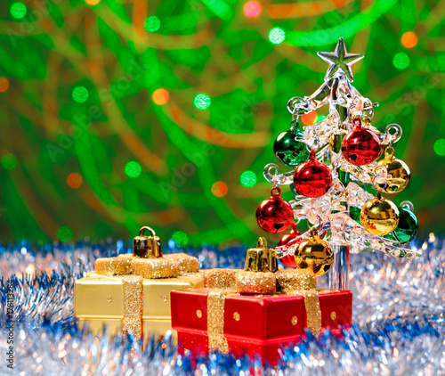 Glass christmas tree standing in the sparkling tinsel with christmas decorations on background with blurred lights