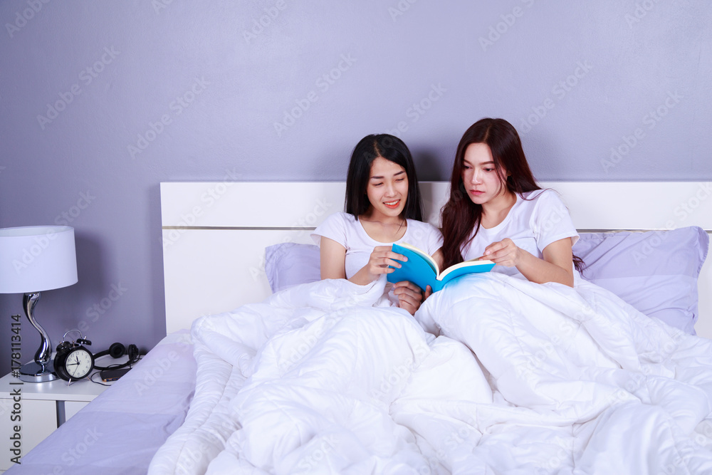 Fototapeta premium two woman reading a book on bed in bedroom