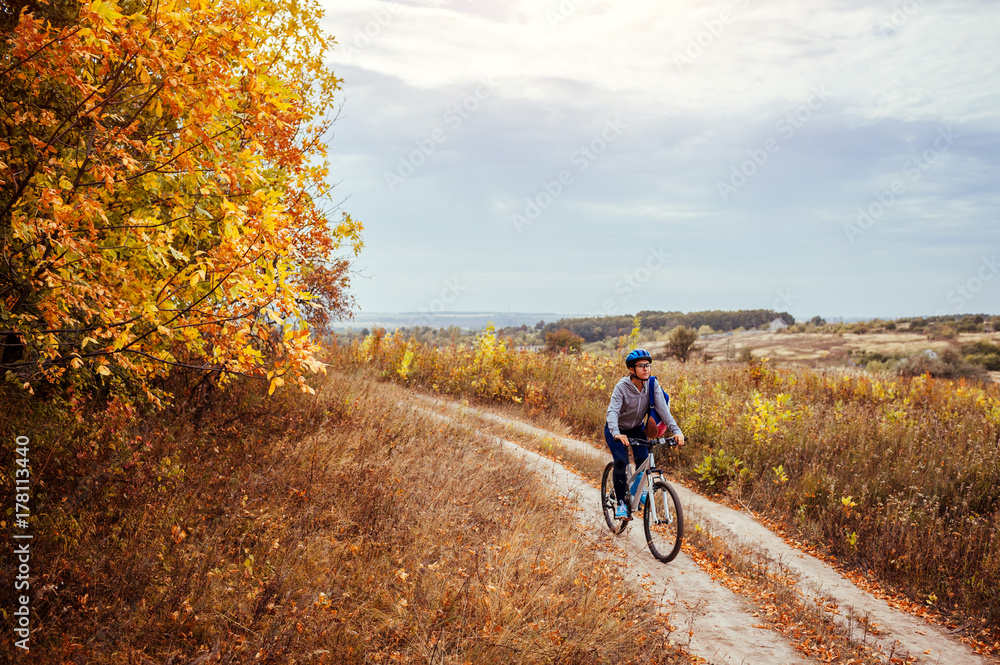 Naklejka premium Young woman riding a bicycle in the autumn field