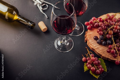 Two glasses of wine with a bottle, corkscrew and grapes