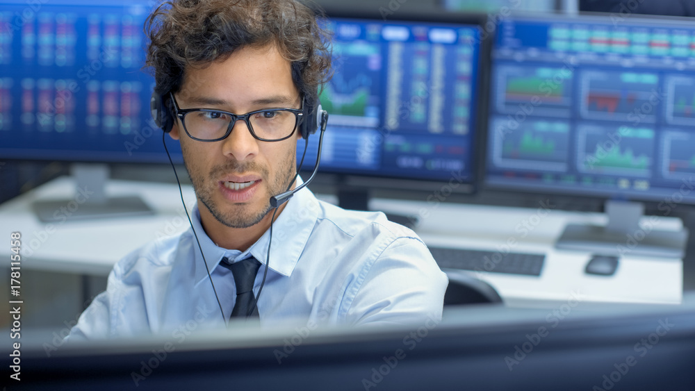 Broker Making Sales with a Headset with His Multi-Ethnic Team of Stock Traders at the Stock Exchange Firm Office is Busy Selling and Buying Bonds and Shares. Displays Show Relevant Graphs and Numbers. Broker Making Sales with a Headset with His Multi-Ethnic Team of Stock Traders at the Stock Exchange Firm Office is Busy Selling and Buying Bonds and Shares. Displays Show Relevant Graphs and Numbers.