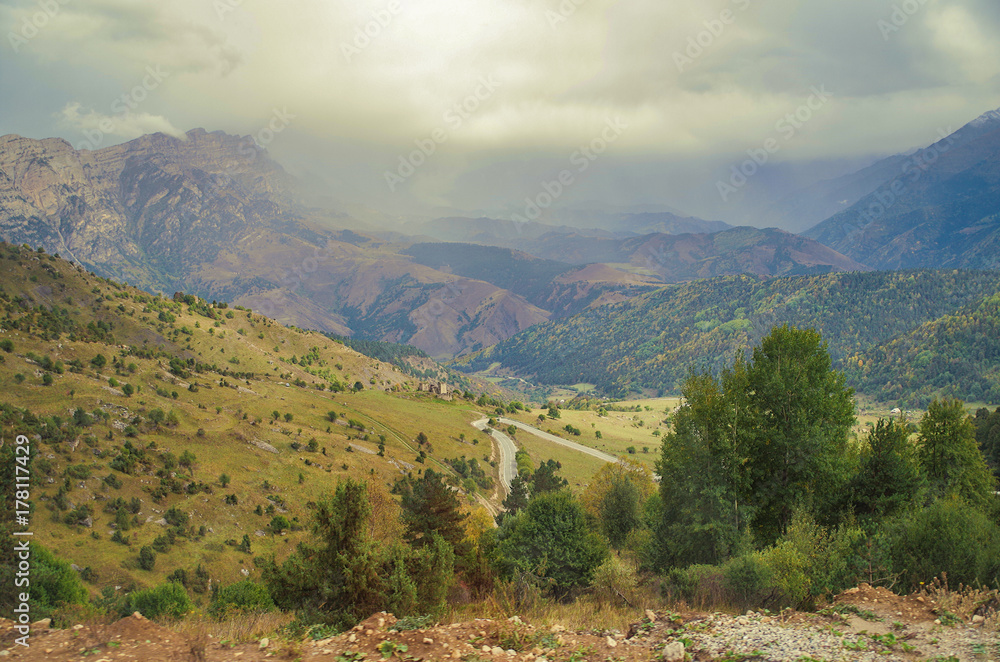 Autumn in the mountains of the Caucasus. Scenic view of the valley after a rain. Empty winding road on the background of the dramatic rainy sky and mountains. Nature and travel. Russia, Ingushetia