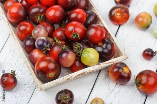 Different tomatoes in the white tray on the wooden background