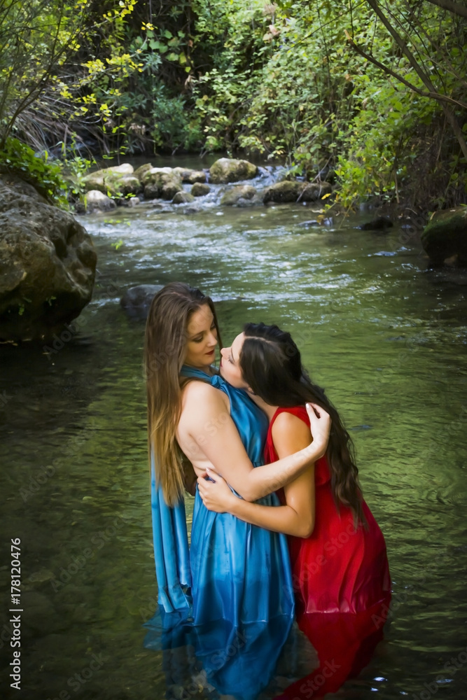 Fototapeta premium Two beautiful women on the bank of a mountain river with evening dresses