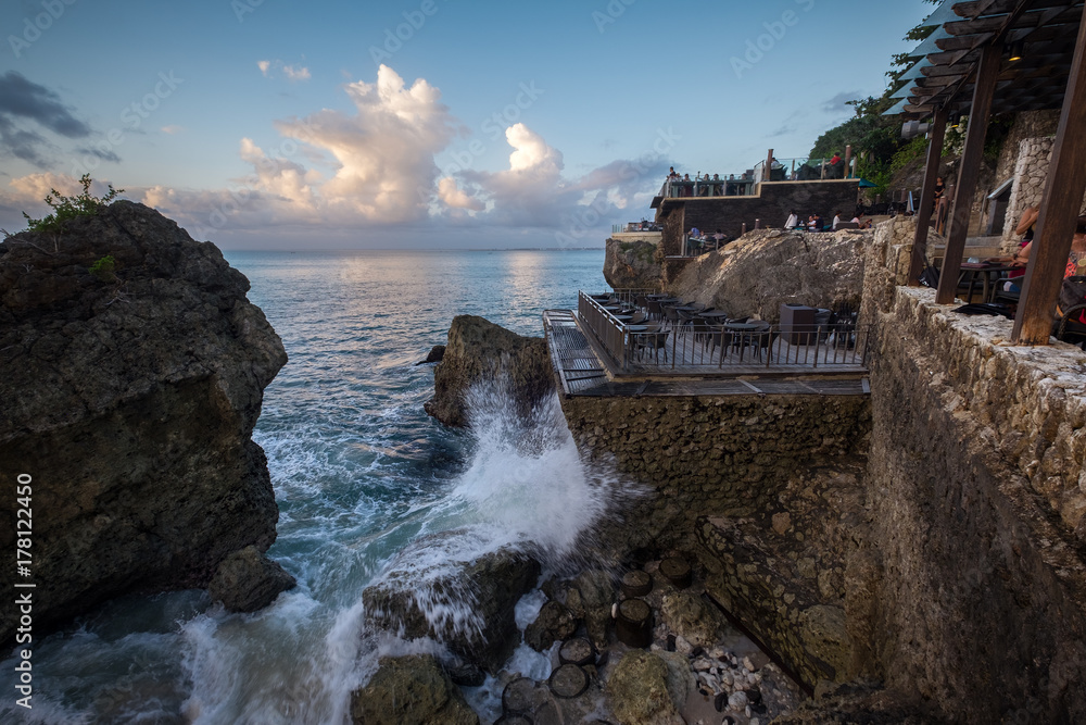 Bali, Indonesia - August 1, 2017: People eating in outdoor terrace during sunset  at Coastline Of  famous Rock Bar in Bali, Indonesia