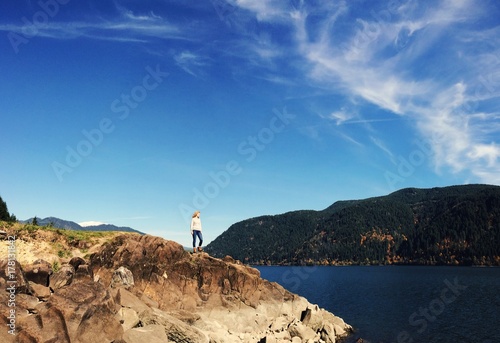 Girl standing on cliff surrounded by mountains and water photo