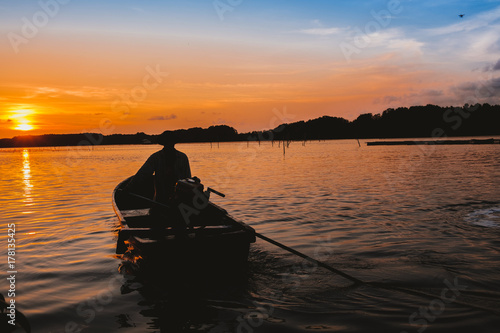a man on long tail boat going into the sun set