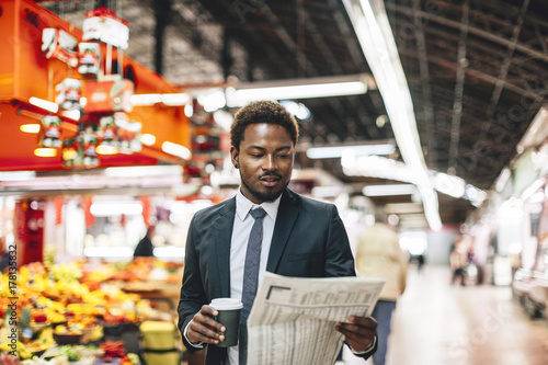 Modern black businessman with newspaper and coffee on a market. photo