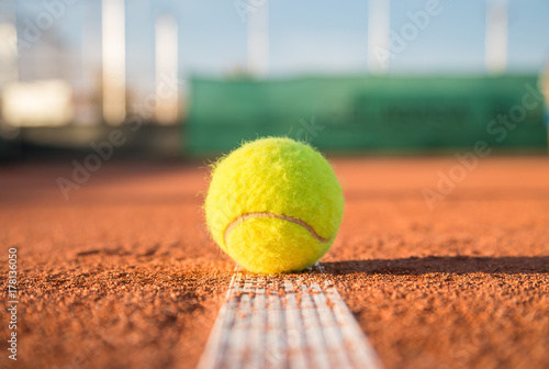 Small tennis ball lying on white line on tennis court on sunny day.  © pablobenii