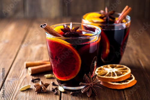 Two glasses of christmas mulled wine with oranges and spices on wooden background.