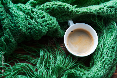 Top view of cup of hot coffee and warm green scarf. Concept of coziness and warmth