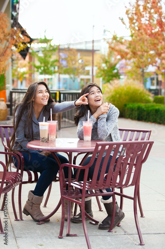 Two teen girls at outdoor cafe drinking boba tea together