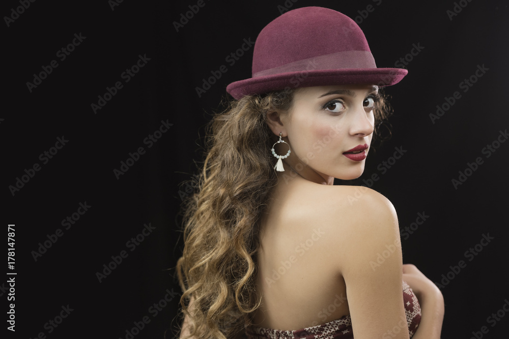 Cute young woman with red lips and long curly hair wear hat and strapless dress in studio black background Cute young woman with red lips and long curly hair wear hat and strapless dress in studio black background