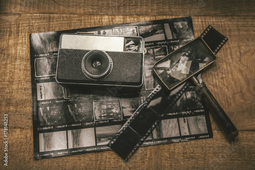 Old analog camera, film, magnifying glass and contact sheet over wooden table. photo