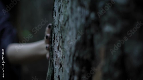 pale witch hand with sharp black nails is touching a trunk of old tree in a dark forest, close-up photo