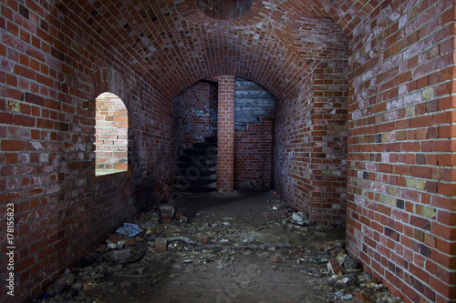 Arched corridor of the old Prussian fortress of red brick, ending with a spiral staircase