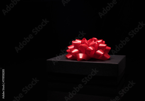 Black gift box on a black surface with big red bow. Close up. Celebrate concept, New Year, Merry Christmas, Anniversary,Birthday,Valentines day,men,women, winter holidays.