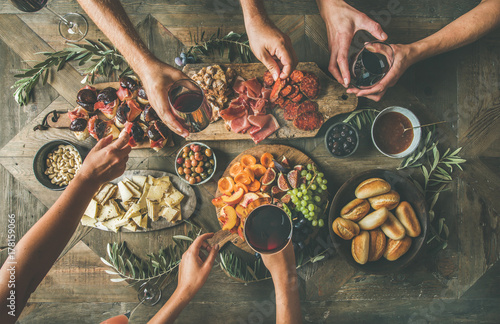 Flat-lay of friends hands eating and drinking together. Top view of people having party, gathering, celebrating together at vintage wooden rustic table set with different wine snacks and fingerfoods