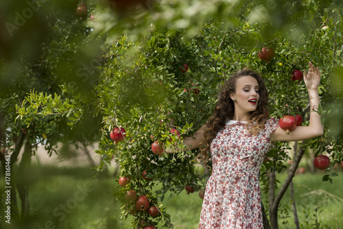 Young woman wearing floral long dress standing against pomegranate trees photo