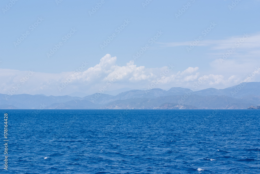 Rocky hills on the horizon under the clouds in the blue sea