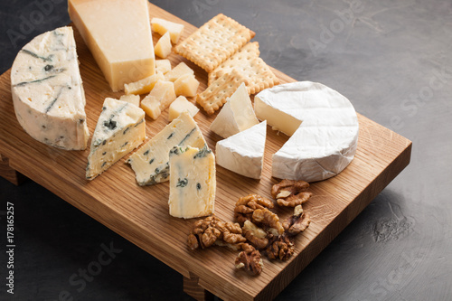 Tasting cheese dish on a wooden plate with walnuts and crackers. Food for wine and romantic, cheese delicatessen on a dark stone table