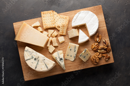 Tasting cheese dish on a wooden plate. Food for wine and romantic, cheese delicatessen on a dark stone table. Top view photo