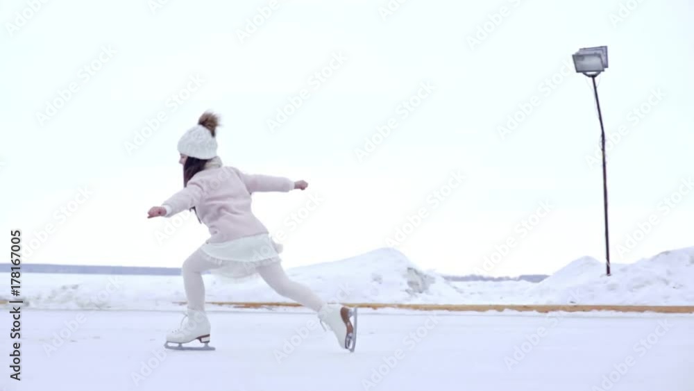 Tracking of adorable girl in pink coat and warm hat ice skating on outdoor rink in winter, then practicing shotgun spin and falling down; little boy having fun in background Tracking of adorable girl in pink coat and warm hat ice skating on outdoor rink in winter, then practicing shotgun spin and falling down; little boy having fun in background