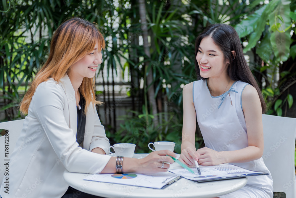 Two businesswomen discussing over graphic paperwork on the table. Two businesswomen discussing over graphic paperwork on the table.