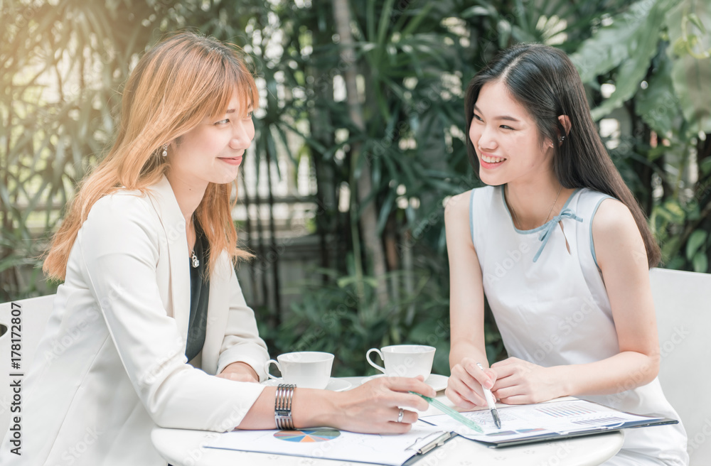 Two businesswomen discussing over graphic paperwork on the table. Two businesswomen discussing over graphic paperwork on the table.
