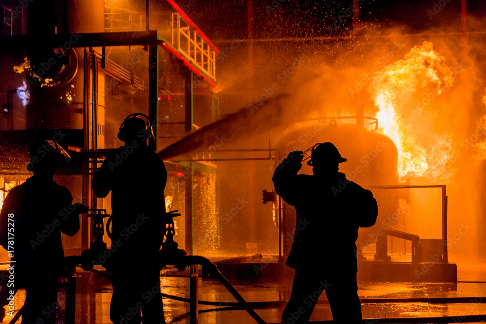 Obraz premium Firemen using water from hose for fire fighting at firefight training of insurance group. Firefighter wearing a fire suit for safety under the danger case.