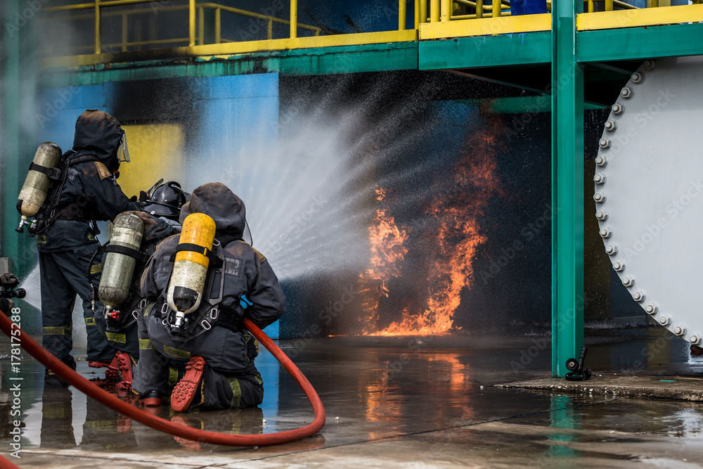 Fototapeta premium Firemen using water from hose for fire fighting at firefight training of insurance group. Firefighter wearing a fire suit for safety under the danger case.