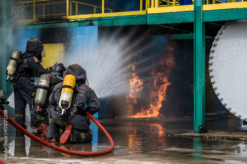 Firemen using water from hose for fire fighting at firefight training of insurance group. Firefighter wearing a fire suit for safety under the danger case.