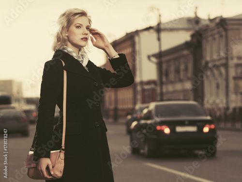 Fashion blond woman in black coat with cross body bag walking in city street © Wrangler