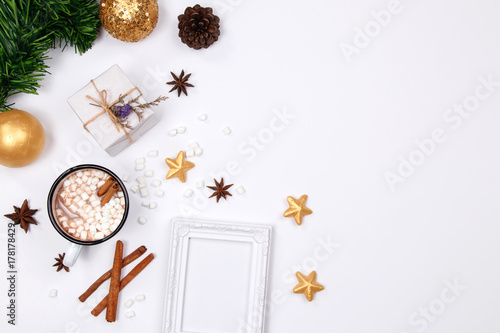 Christmas frame made of pine branches, pine cone, cup of hot chocolate drink with marshmallows, cinnamon sticks, anise star, gift box and golden ornaments on white background. flat lay, top view.