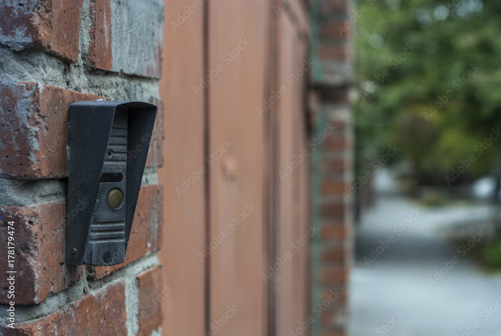 The button on the intercom mounted on the brick wall