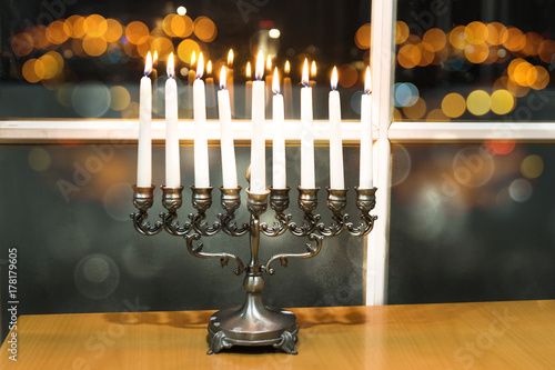 Happy Hanukkah. Low key image of jewish holiday Hanukkah with menorah by the window with the night view out of focus on Tel Aviv, Israel