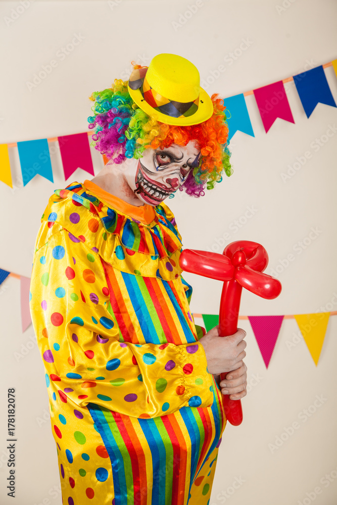 a terrible clown. Halloween. A crazy clown with a balloon in the form of a flower. Childish fear a terrible clown. Halloween. A crazy clown with a balloon in the form of a flower. Childish fear