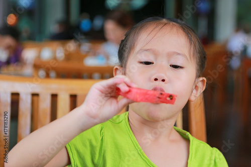 Asian little girl eating slice of watermelon at the restaurant.