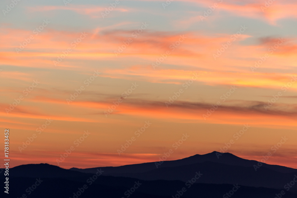 A silhouette of a mountain peak at sunset, under a big sky with beautiful, striped red clouds