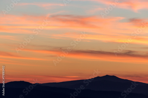 A silhouette of a mountain peak at sunset, under a big sky with beautiful, striped red clouds