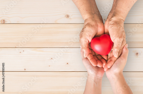 Fototapeta Elderly senior person or grandparent's hands with red heart  in support of nursi