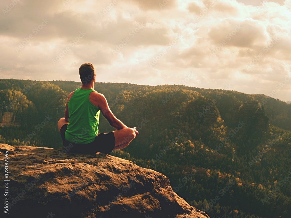 Man meditating in Lotus Pose on rocky cliff. Sportsman practicing Yoga on stone edge