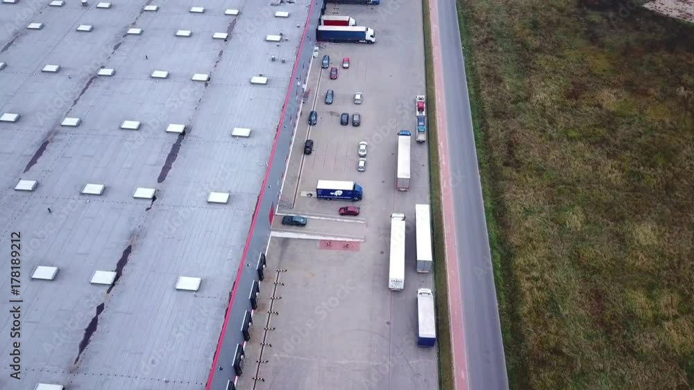 Trucks are Driving to Logistics Center. Aerial Shot./ Storage Building/ Loading Area where Many Trucks Are Loading/ Unloading Merchandise Trucks are Driving to Logistics Center. Aerial Shot./ Storage Building/ Loading Area where Many Trucks Are Loading/ Unloading Merchandise