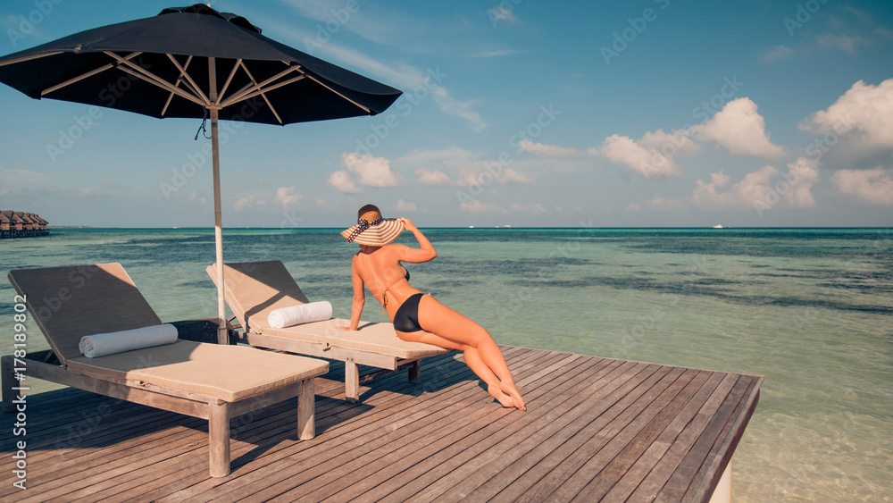 Perfect beach vacation for summer travel background. Relaxed woman wearing sun hat and bikini on a palm trees with the blue sea view from above. Exotic travel destination and tropical holidays concept