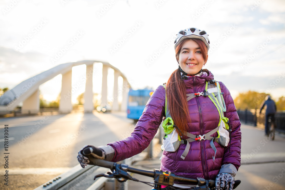 Photo of sportive woman in helmet on bicycle on bridge in city