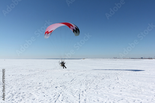 Man with a parachute and a motor, flying in the sky on a winter day over a frozen river