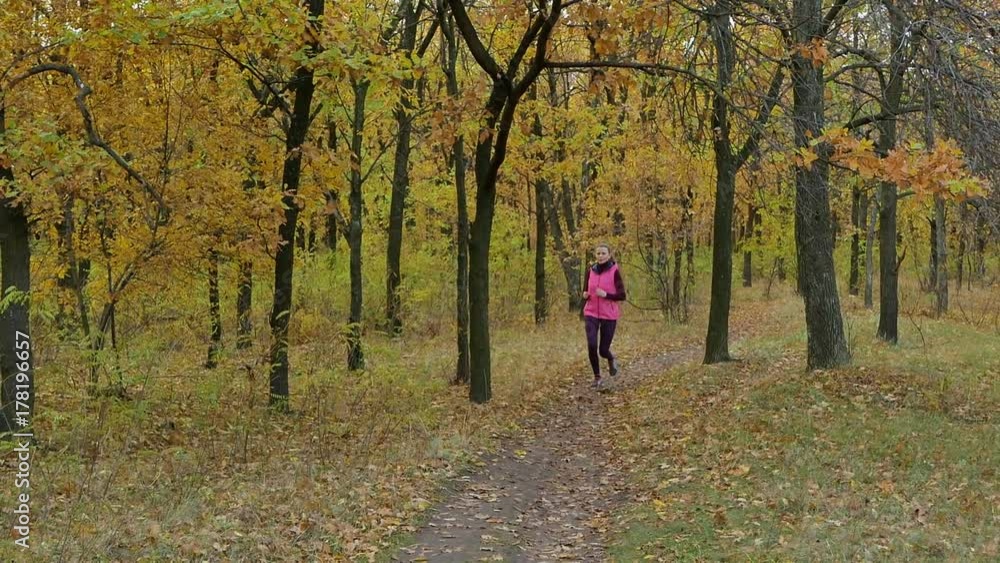 Slow motion Running - woman runner jogging on autumn forest path. Fit female sport fitness model athlete trail running training. Runner gril in sportswear running in park exercising outdoors. Slow motion Running - woman runner jogging on autumn forest path. Fit female sport fitness model athlete trail running training. Runner gril in sportswear running in park exercising outdoors.